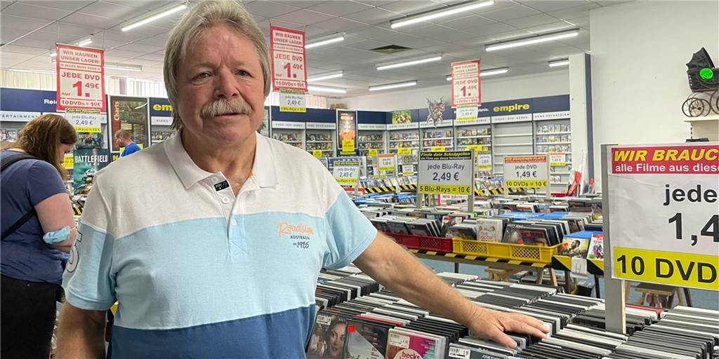 Dortmunds letzte Videothek schließt: Betreiber (69) startet Ausverkauf Mann steht vor einem Aufsteller mit DVDs