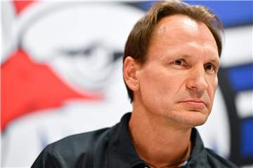 Adler Mannheims Trainer Pavel Gross sitzt auf dem Podium vor einem Vereinswappen. Foto: Uwe Anspach