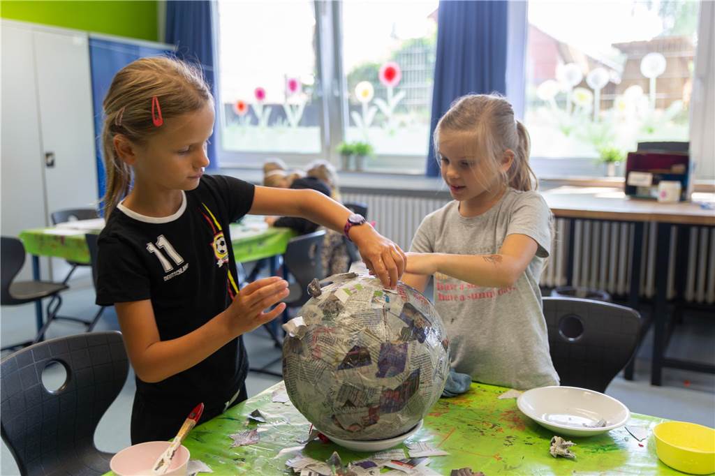Ferien in der OGS Grafenwald: Kinder baden jetzt in 10.000 Bällen Zwei Mädchen basteln Astronautenhelme.