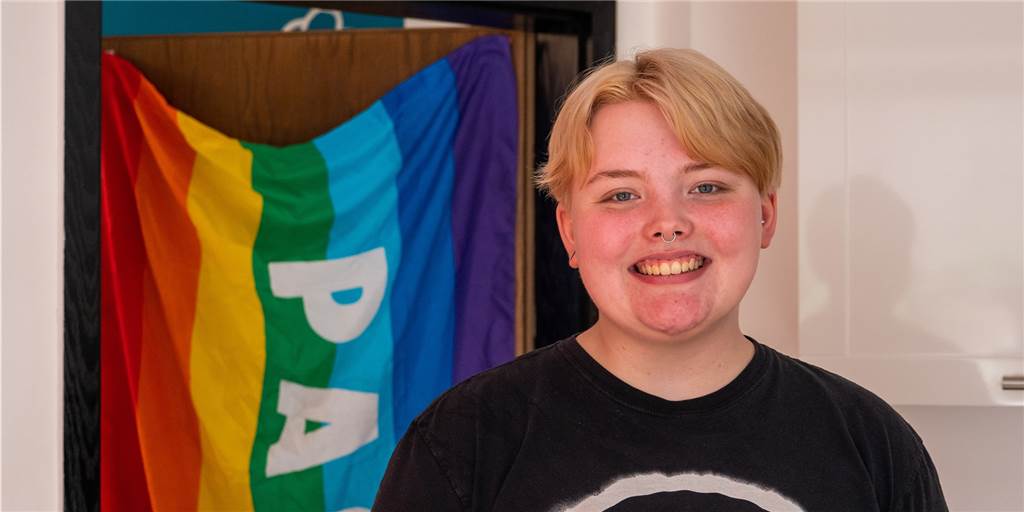 Als Mädchen geboren: Alex Terheyden fühlt sich gefangen im falschen Körper Alex Terheyden steht vor einer Regenbogenflagge und lächelt in die Kamera,