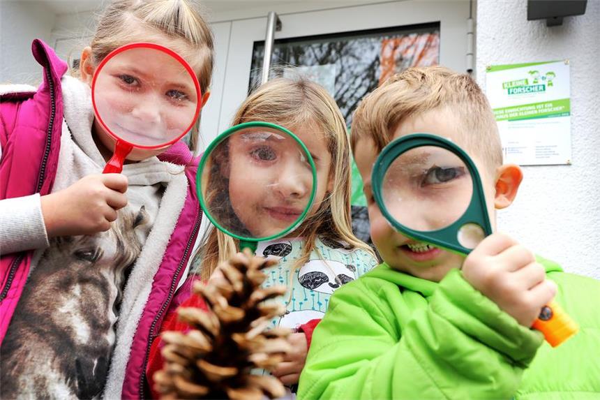 Kita wird zum "Haus der kleinen Forscher" Aliyah, Emma und Eren schauen sich vor dem "Haus der kleinen Forscher" mit Lupen einen Tannenzapfen an.