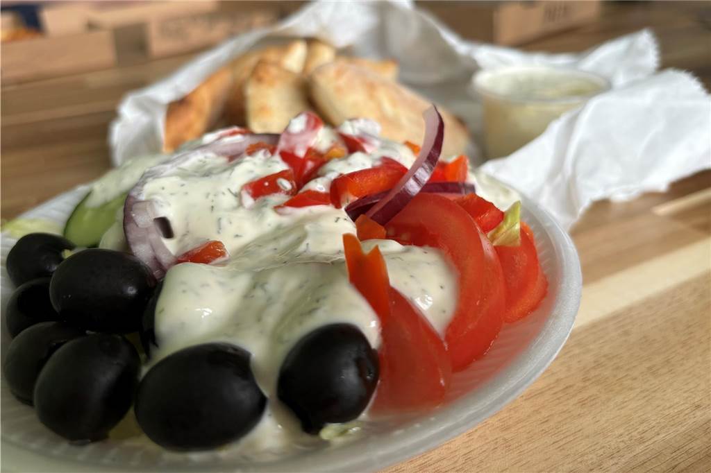 Zwischen Pizza und indischen Speisen: Il Rustico überzeugt im Test Ein gemischter Salat mit Oliven, Tomaten, Gurken, roten Zwiebel und Dressing steht vor einigen Pizzabrötchen und Knoblauch-Sauce.
