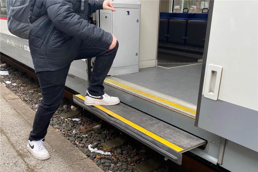 Ein junger Mann steigt vom Bahnsteig in einen Zug ein und muss dabei eine hohe Stufe hinaufgehen.