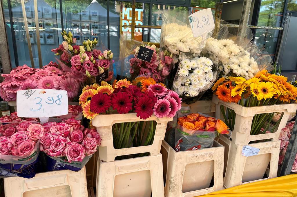 Christina Zapler (62) kam durch die Liebe zum Wochenmarkt Rosen und Sonnenblumen sind in Körben und stehen zum Verkauf bereit. Preisschilder sind an den Körben befestigt.