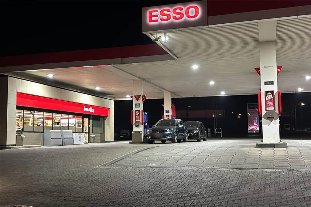 Tankstellenpächter zwischen Schock und Erleichterung Außenansicht einer Esso-Tankstelle im Dunkeln. Zwei schwarze Autos stehen vor Zapfsäulen.