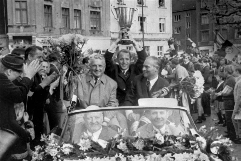 Selbst genähte Fahne erlebte vor 55 Jahren den Europapokalsieg des BVB Am Tag nach dem Europapokalsieg fuhr der BVB in einem Autokorso in Dortmund durch ein Spalier jubelnder Menschen. Im Wagen zu sehen sind (v.l.) Trainer Willy Multhaup, Kapitän Wolfgang Paul mit dem Pokal und Klubpräsident Stork.