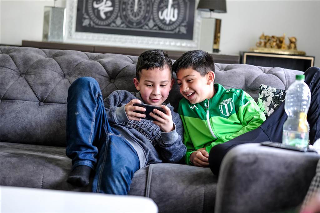 Nach Zugunglück im Februar: Amir (9) ist endlich wieder zu Hause Zwei Jungs sitzen auf einem Sofa in Recklinghausen und schauen sich Videos auf einem Handy an