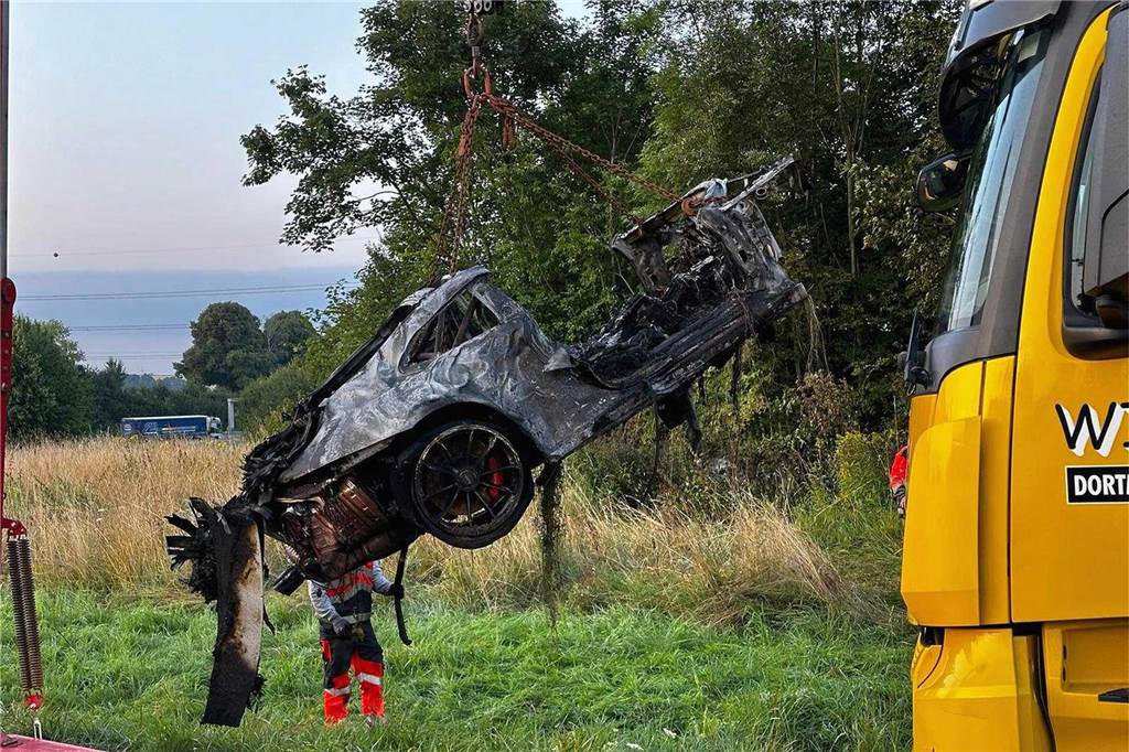 An der Unfallstelle im Kreuz Dortmund/Unna von A44 und A1 birgt ein Kran den ausgebrannten Porsche aus dem Grünstreifen.
