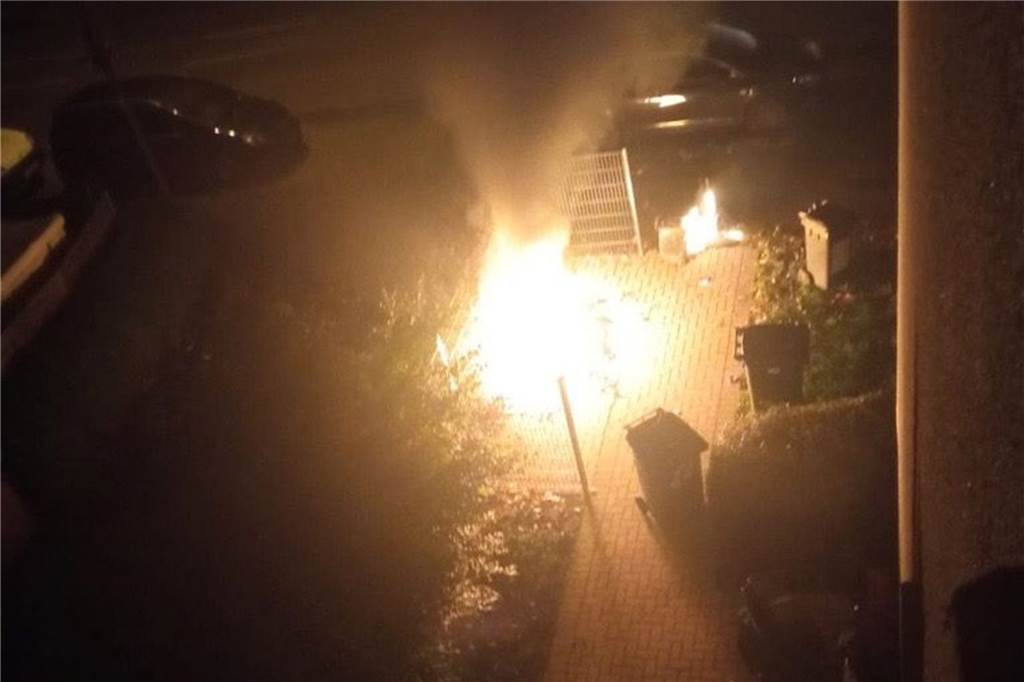 Vom Knistern der Flammen geweckt: So haben Anwohner die Mülltonnen-Brände erlebt Mehrere Mülltonnen brennen. Eine dunkle Rauchwolke steigt in Richtung Himmel.