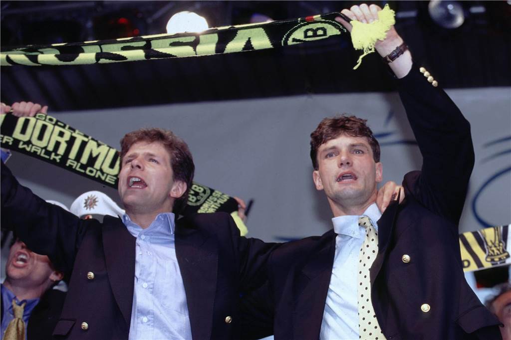 Andreas Möller und Michael Zorc halten einen BVB-Schal in den Händen.
