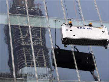 Arbeiter säubern im Geschäftsviertel in Peking die Fenster eines Einkaufszentrums, in denen sich ein im Bau befindliches Hochhaus spiegelt. Foto: Andy Wong/Illustration