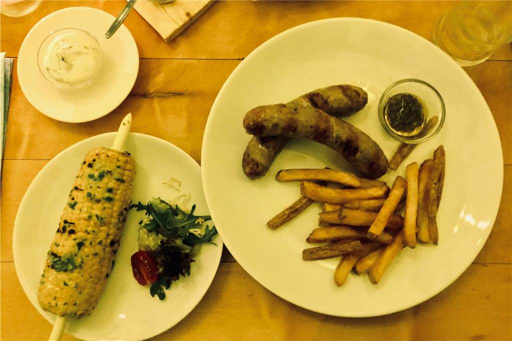 Argentinische Wurst mit Pommes und dazu ein mit Kräuterbutter übergossener gegrillter Maiskolben.