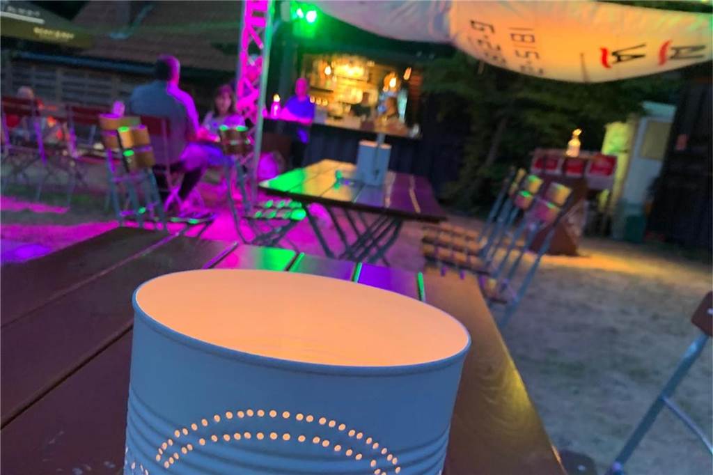 Auf dem Foto sieht man Gäste in einem schön beleuchteten Biergarten am Abend.