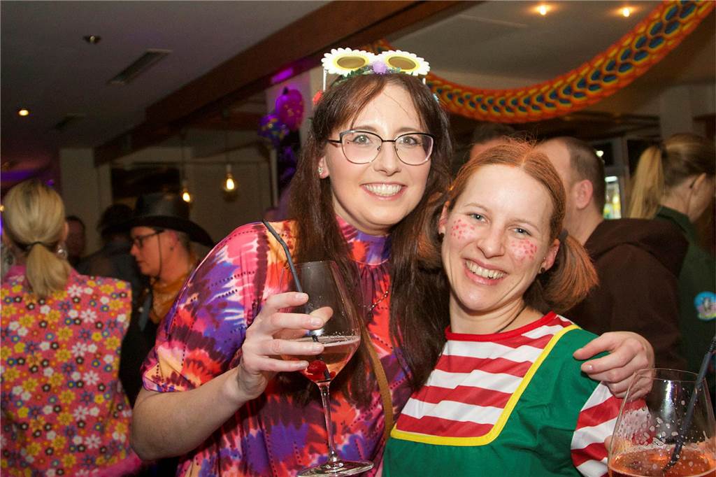 Hier finden Karnevals-Partys und Weiberfastnacht statt Zwei verkleidete Frauen schauen in die Kamera und lachen, die eine hält ein Weinglas in der Hand.