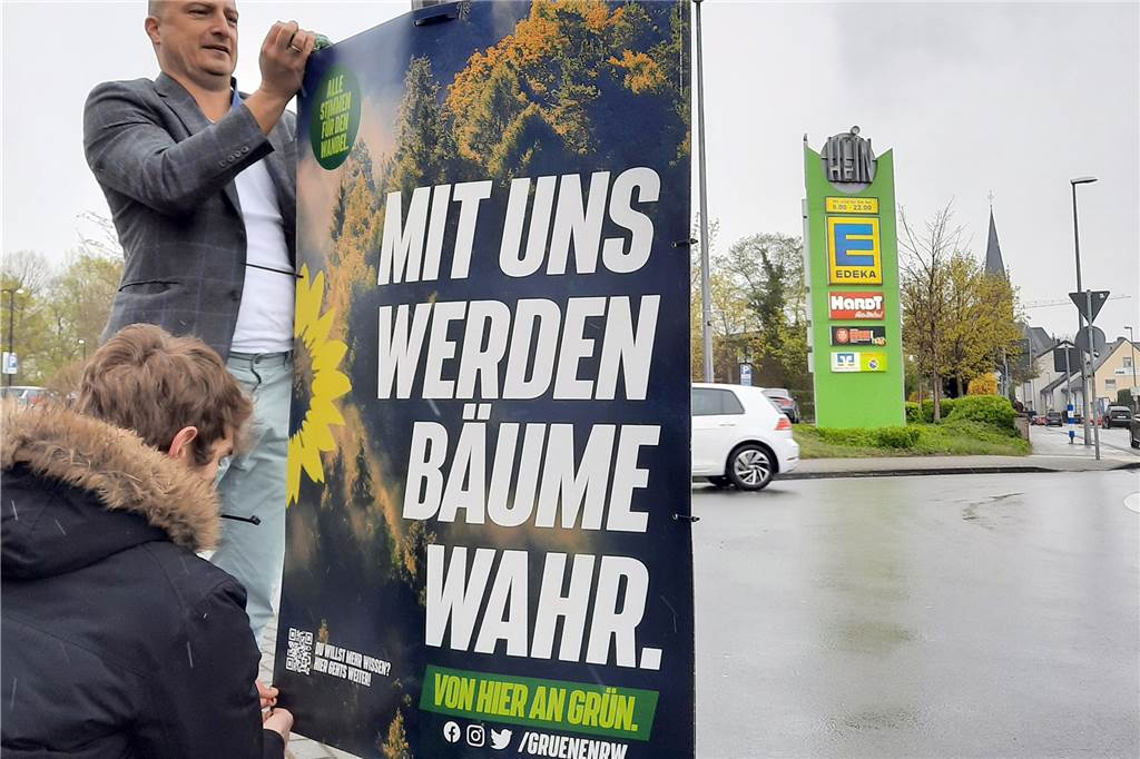 NRW-Grüne klauen „Hoch-die-Hände“-Slogan für Landtagswahl – Wie reagiert der Sänger? Zwei Parteimitglieder der Grünen hängen in NRW ein Plakat mit der Aufschrift "Mit uns werden Bäume wahr" auf.