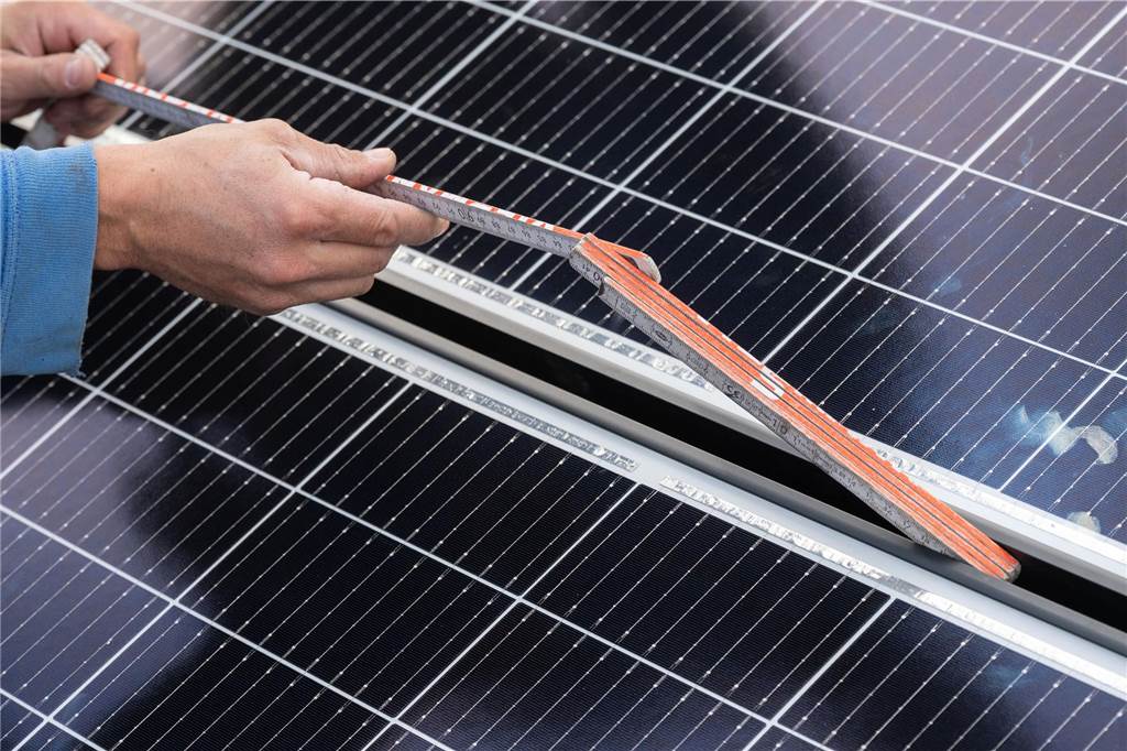 Stadt weist auf neue Regeln für Wärmepumpen, Solar- und Windanlagen hin Ein Mann vermisst eine Solarzelle mit einem Zollstock.