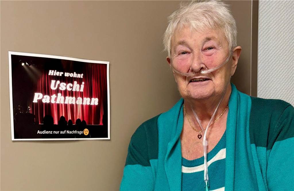 Uschi Pathmann steht vor einer Tür mit ihrem Namensschild und der Aufschrift „Audienz nur auf Nachfrage". 