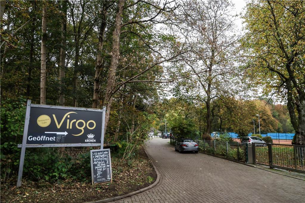 Ein Schild auf der linken Bildhälfte weist auf das Restaurant Virgo hin. Rechts ist in der Ferne ein Tennisplatz zu erkennen.