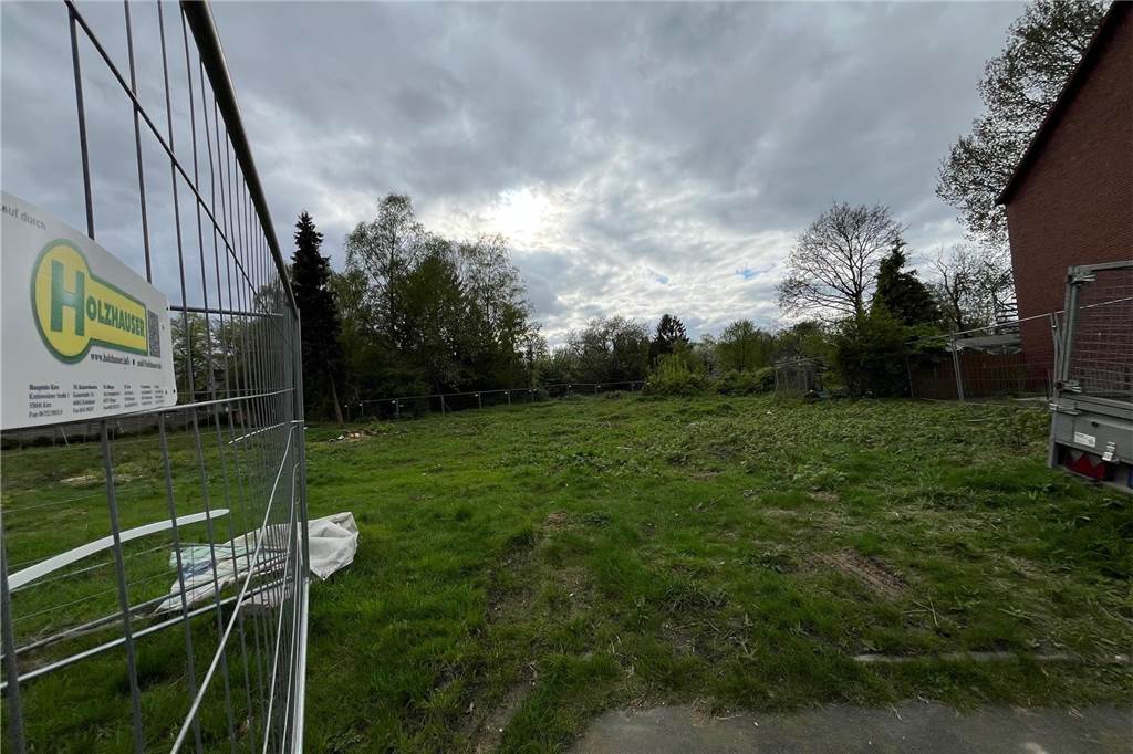 Immobilien: Hier können Bürger den Traum vom Eigenheim verwirklichen Links ist ein Bauzaun, dahinter ein Grünstreifen und rechts daneben ein Wohnhaus zu sehen.
