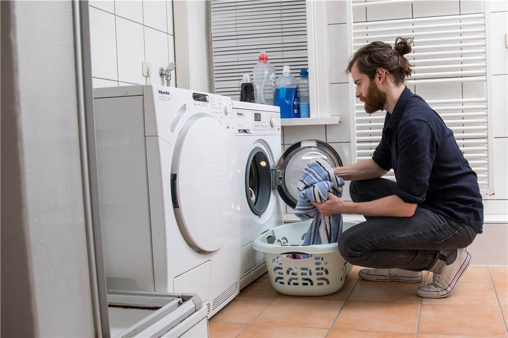 Ein Mann belädt eine Waschmaschine mit Wäsche.