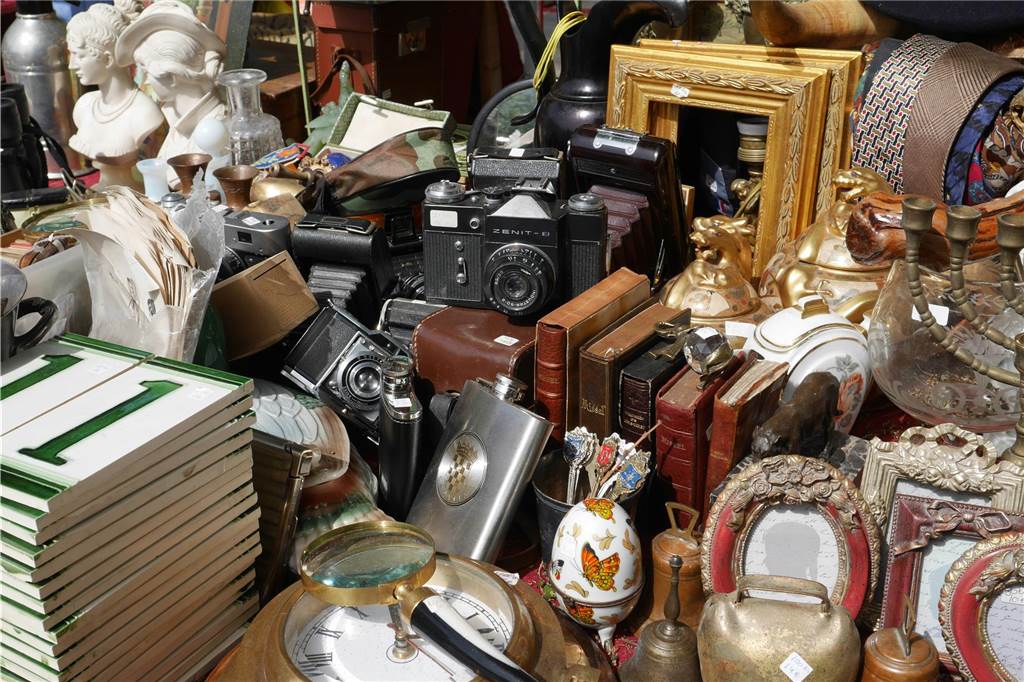 Trödelmarkt in NRW am Wochenende: Wo ist am 12. und 13. April 2025 Flohmarkt? Auf einem Trödelmarkt-Stand liegen verschiedenste Gebrauchtwaren - unter anderem Uhren, Bilderrahmen, eine Kamera, eine Lupe, Skulpturen, Bücher und mehr.
