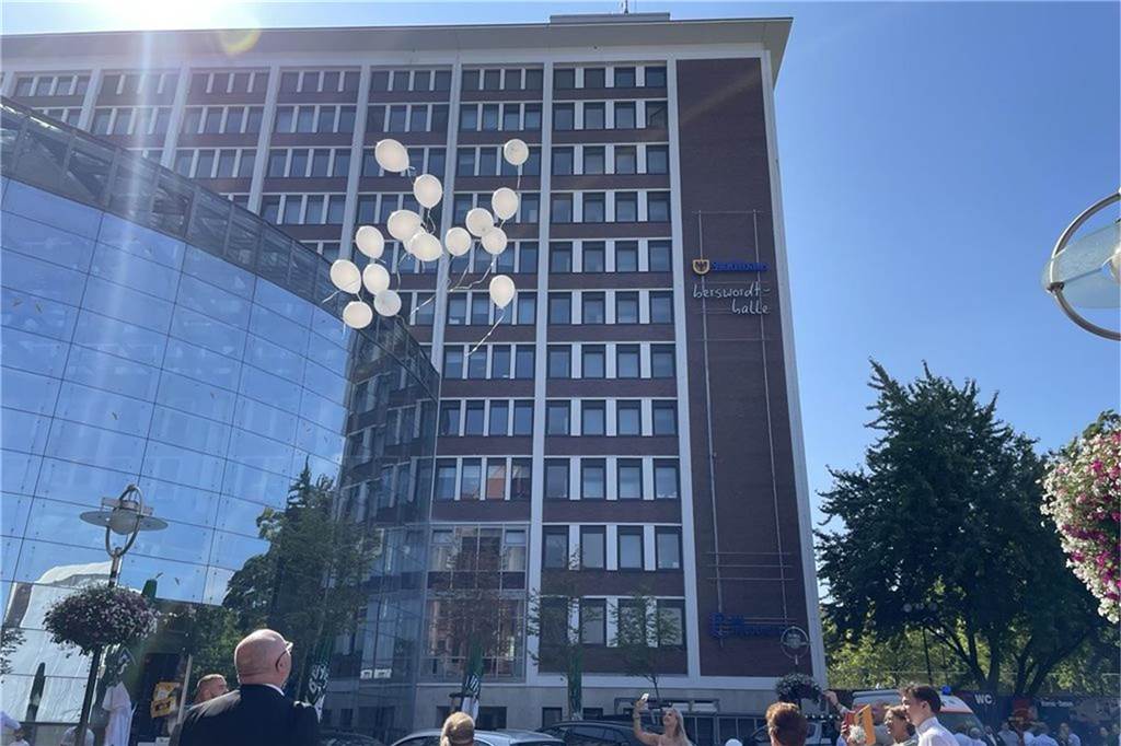 Aus dem Geschenk fliegen weiße Heliumballons in den Himmel über dem Dortmunder Friedensplatz. Die Gäste schauen ihnen hinterher. 