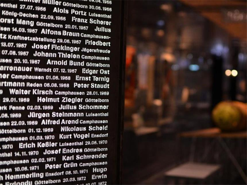 Unter Tage: Reise durch die Bergbau-Geschichte an der Saar Ausstellung «Das Erbe»: Eine Tafel erinnert an 2000 unter Tage getötete Arbeiter. Im Hintergrund ist eine Rettungsbombe zum Bergen von Toten und Verletzten aus dem Schacht zu sehen. Foto: Jörg Fischer