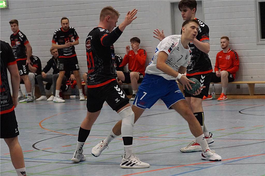 SG Handball Kamen vermeldet Doppel-Verstärkung: Rückkehrer und Neuzugang für den Bezirksligisten Bastian Stremmer (in Weiß) hat einen Handball in der Hand. Zwei Spieler in Schwarz stören ihn nicht wirklich, sodass er jeden Moment ungehindert werfen kann.