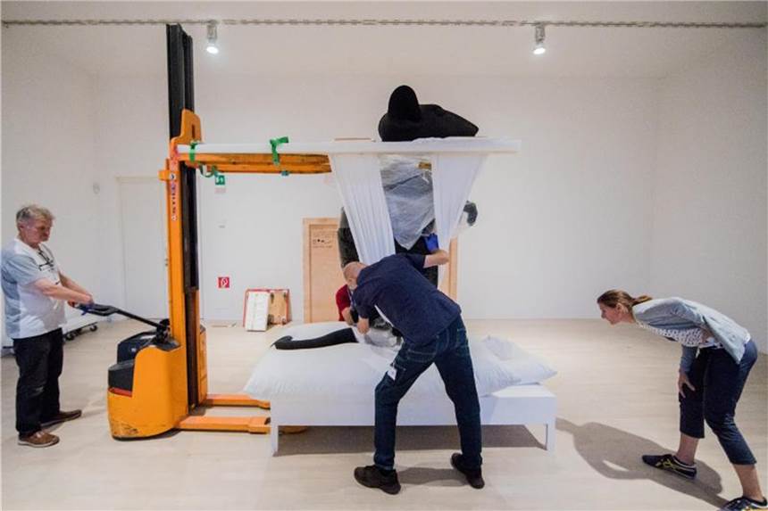 K21 Ständehaus: Gegenwartskunst neu präsentiert Behutsam wird die schwarze Riesenmaus aus dem Werk „Mann und Maus“ der Künstlerin Katharina Fritsch auf ein Bett heruntergelassen. Foto: Rolf Vennenbernd