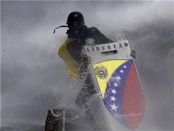 Bei Anti-Regierungs-Protesten in der venezolanischen Hauptstadt Caracas schützt sich ein Demonstrant mit einem selbstgebauten Schild vor einem Wasserwerfer. Foto: Ariana Cubillos