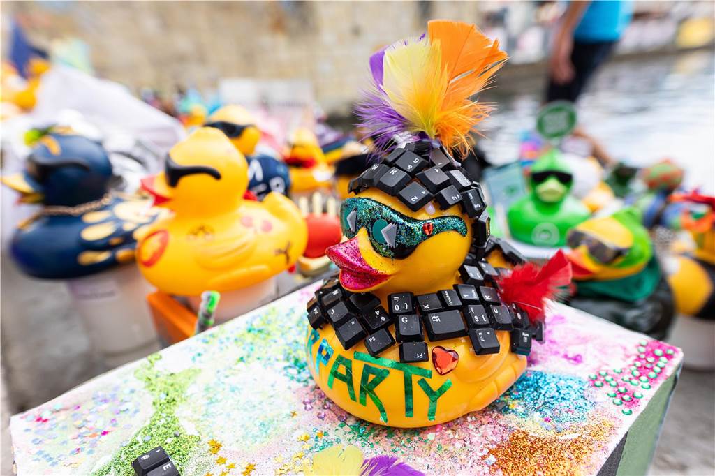 Veranstaltungen am Wochenende: Kneipennacht, Entenrennen, Travestie Eine gelbe Gummiente, geschmückt mit glitzernden Accessoires, Federn und Tastaturtasten, steht im Vordergrund. Im Hintergrund sind weitere dekorierte Gummienten verschiedener Farben und Stile erkennbar.