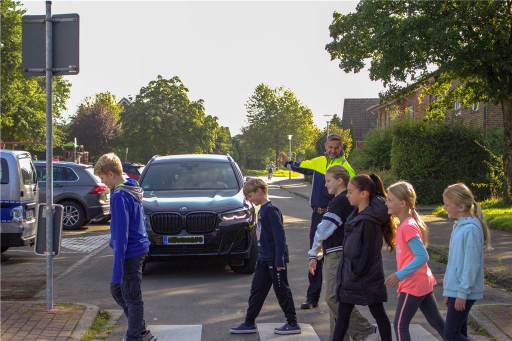 Verkehrssicherheit an Schulen: Raser bekommen selbst gemalten Denkzettel Polizist hilft Kindern über den Zebrastreifen.