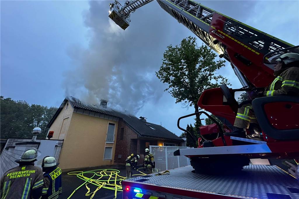 Feuer in Menden: Ein Toter bei Brand in Einfamilienhaus Feuerwehrfahrzeug und Einsatzkräfte vor brennendem Haus in Menden