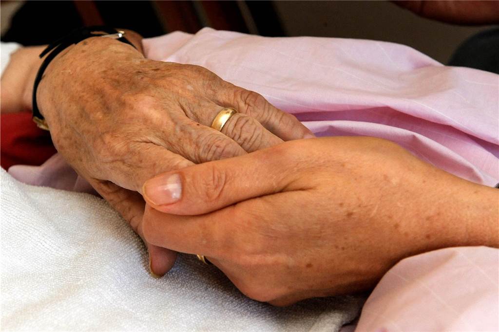 Evri (63) und Helmut (66) Stiller sind Sterbebegleiter: „Lachen mehr als man denkt“ Eine Person hält die Hand eines sterbenden Menschen.