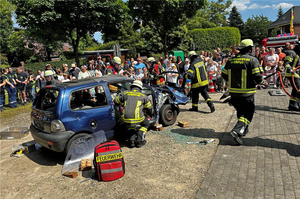 Feuerwehrleute zerlegen ein Auto, während viele Menschen dabei zuschauen.