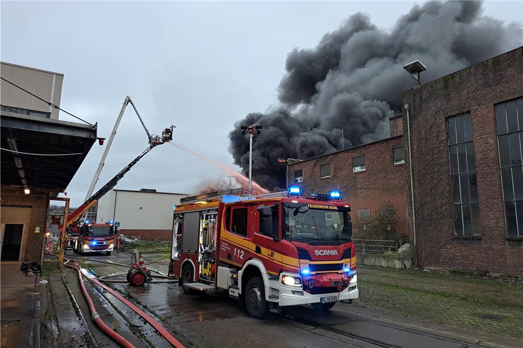 Großbrand auf AV 3/7: Bürogebäude brennt Ein Feuerwehrwagen steht vor einem Gebäude auf dem Gelände der ehemaligen Zeche Auguste Victoria (AV) in Marl, über dem eine große dunkle Rauchwolke zu sehen ist.
