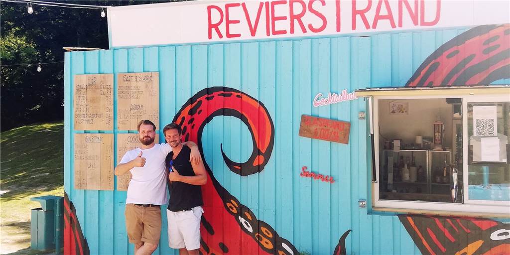 „Lecker Eis, Cocktails, frisch gezapftes Bier und vieles mehr“, damit werben Jens Röhmer und Adrian Busch auf den eigens bemalten Schildern an den Pforten des Revierstrandes