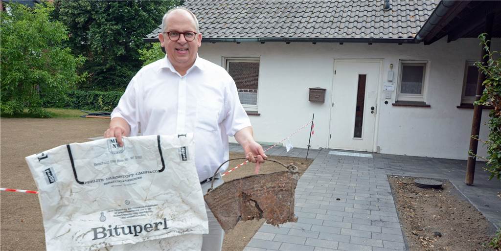 Pfarrer Thorsten Melchert mit zwei "Funden" einer lange zurückliegenden Baumaßnahme. Vom Metalleimer ist nich viel übrig geblieben, auf der Folie findet sich noch die schon lange abgeschaffte vierstellige Postleitzahl von Dortmund. Im Hintergrund ist zu erkennen, dass mit der Umgestaltung die Stufen verschwunden sind.