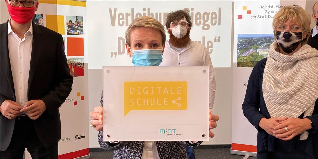 Dieses Gymnasium ist die einzige „Digitale Schule“ in Dortmund HHG-Schulleiterin Susanne Köhnen hält stolz die Auszeichnung in die Höhe. Auch Thomas Westphal (l.), der neue Oberbürgermeister von Dortmund (SPD), und Schuldezernentin Daniela Schneckenburger (Bündnis 90/Die Grünen) freuen sich mit ihr und dem Lehrer Herrn Torka mit – was leider unter den Mund-Nasen-Schutzmasken nicht so deutlich zu erkennen ist.