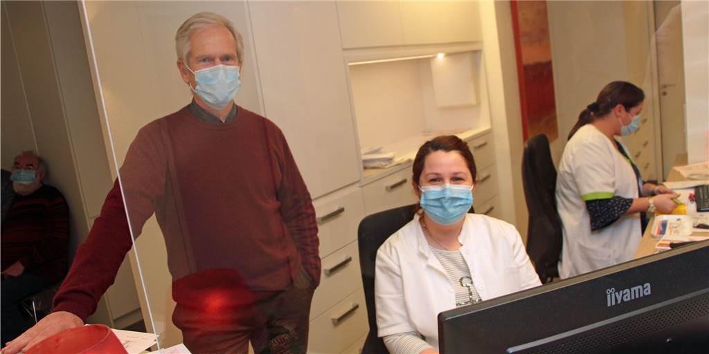 Ärzte-Sprecher zur Corona-Lage: „Deutlich weniger Routine-Checks“ Dr. Hans Piepenbrock mit Mitarbeiterin Radiye Bulut hinter der Plexiglas-Wand in der Praxis an der Alten Münsterstraße.