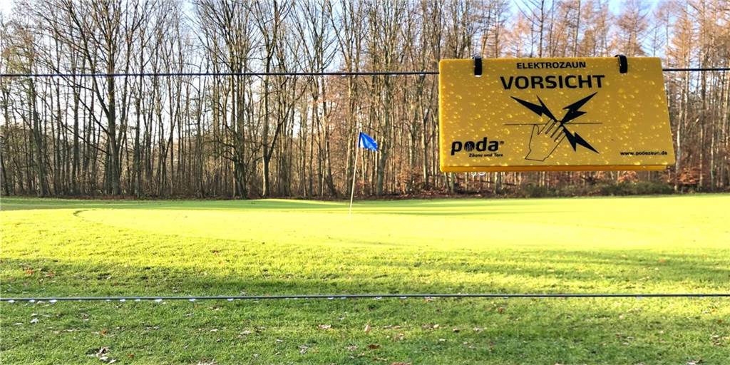 Wildschwein-Abwehr durch Stromstöße: Golfer zäunen Platz im Süden ein „Elektrozaun - Vorsicht": Am neuen Elektrozaun des Golfplatzes warnen Schilder vor den spannungsgeladenen Drähten.