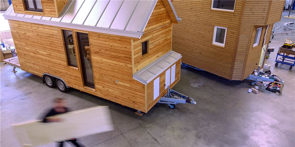 Tiny Houses: Stadtlohn stellt Minihaus-Interessenten vor Entscheidung Ein Mitarbeiter trägt eine Holzplatte durch die Produktionshalle eines Tiny-House-Herstellers. Die Stadt Stadtlohn will sechs Parzellen für Tiny Häuser anbieten – wenn es genügend ernsthafte Nachfragen gibt.