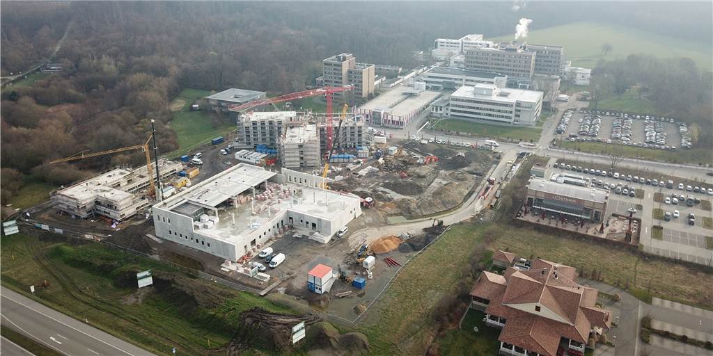 Der Baufortschritt des Gesundheitscampus am EvK ist rasant: Die Großküche (unten), die Kita (links am Bildrand), das Pflegeheim (darüber) sind in weiten Zügen des Rohbaus schon fortgeschritten. Die Erschließungsstraße ist erkennbar. Auf dem Bauland an der Straße neben der L’Osteria wird bald noch die Zentralapotheke gebaut. Im Hintergrund sind die Gebäude des EvK zu erkennen, unten rechts das Café del Sol.