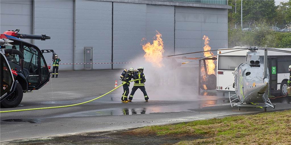 Zwei Feuerwehrleute löschen Flammen aus einem ausgebauten Triebwerk. Daran wird ein echter Brand simuliert.