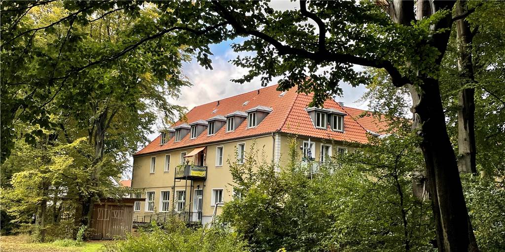 Im Vordergrund befindet sich das städtische Waldgebiet, dahinter das Nachbarschaftshaus, dass Vivawest gehört.