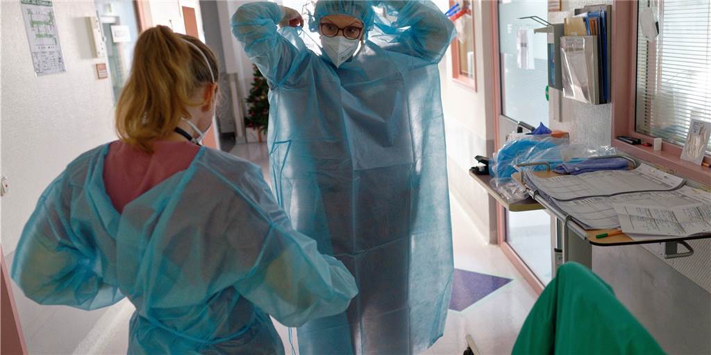 Wie viele Patienten kommen MIT statt WEGEN Corona? Krankenhaus äußert sich Eine Ärztin und eine Pflegerin ziehen Infektionsschutzkleidung an.