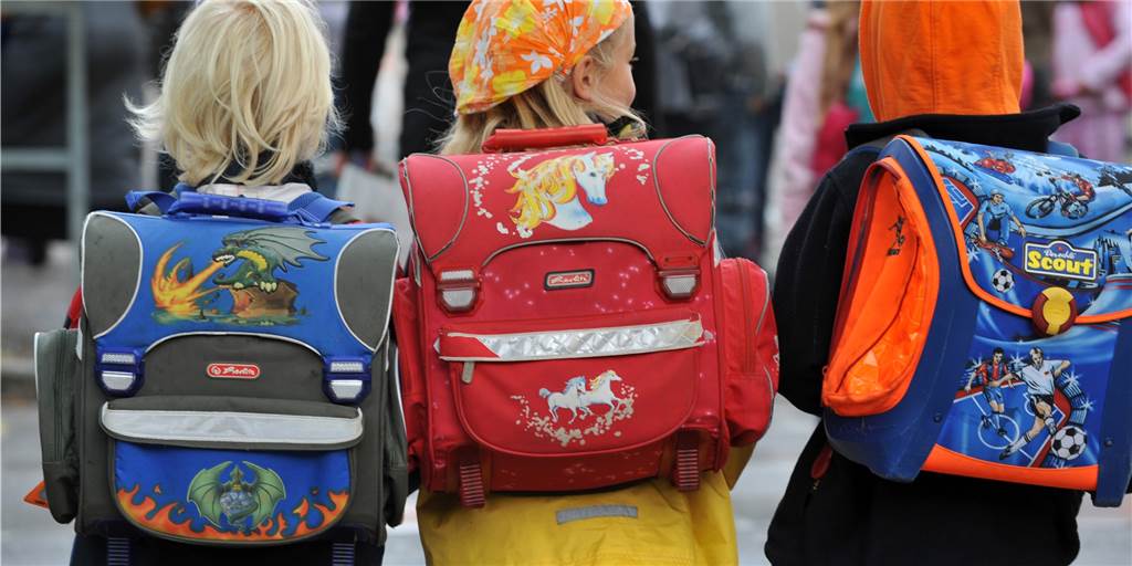 OGS-Plätze werden knapp: Kinder ablehnen oder Kapazitäten erweitern? Drei Kinder laufen mit ihren Schulranzen zur Schule.
