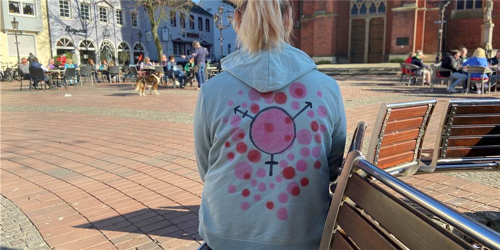 Sonya aus Haltern: „Es ist nicht leicht, in diesem System trans* zu sein.“ Sonya aus Haltern sitzt auf einer Bank vor dem alten Rathaus.
