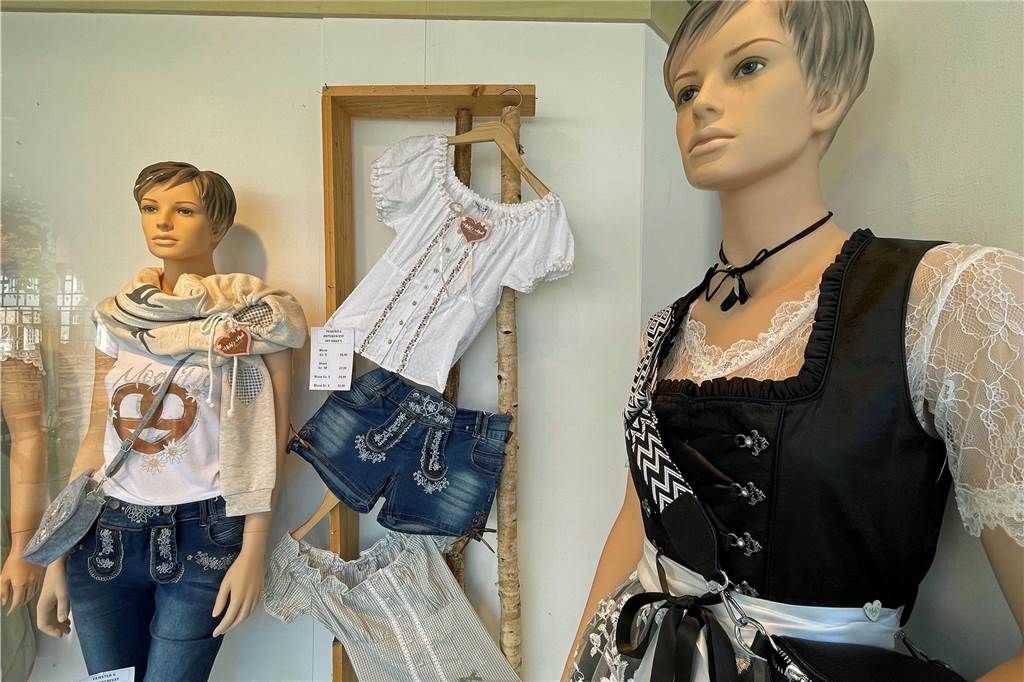 Geschäftsleute schwimmen auf der Oktoberfest-Welle mit Blick in das Oktoberfest-Schaufenster vom Modehaus Kroes mit unterschiedlichen Trachten-Modellen.
