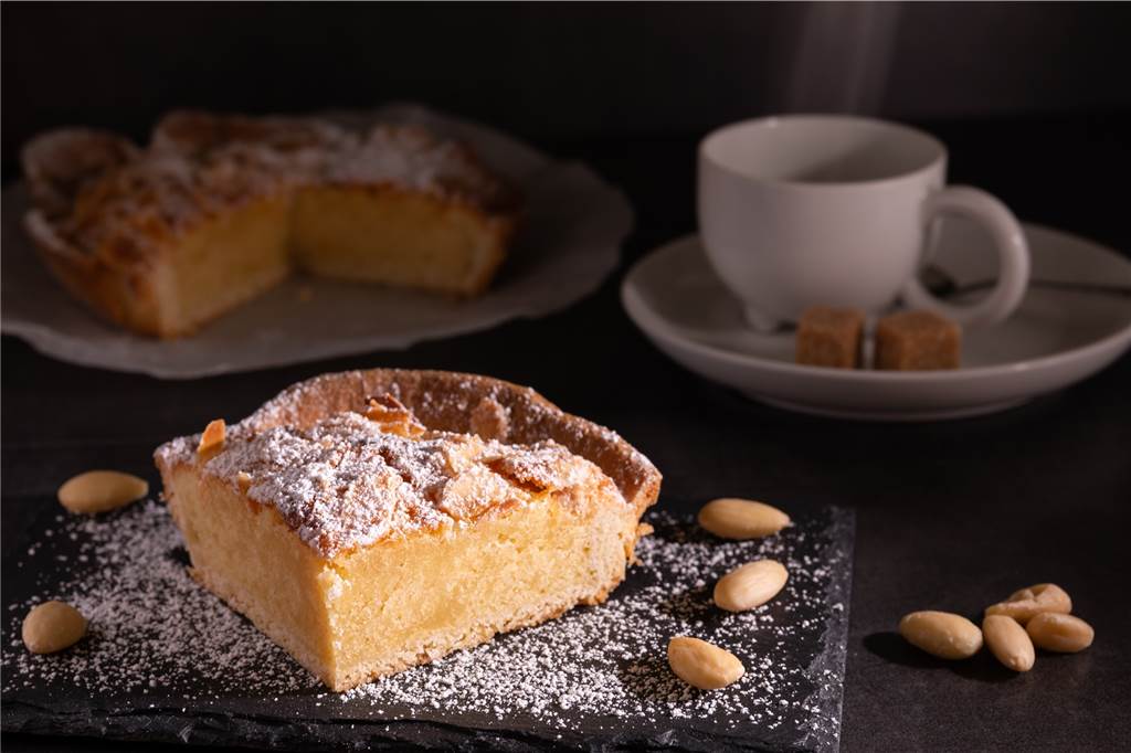 ein stück kuchen, mandeln und ein ganzer kuchen mit kaffee im hintergrund